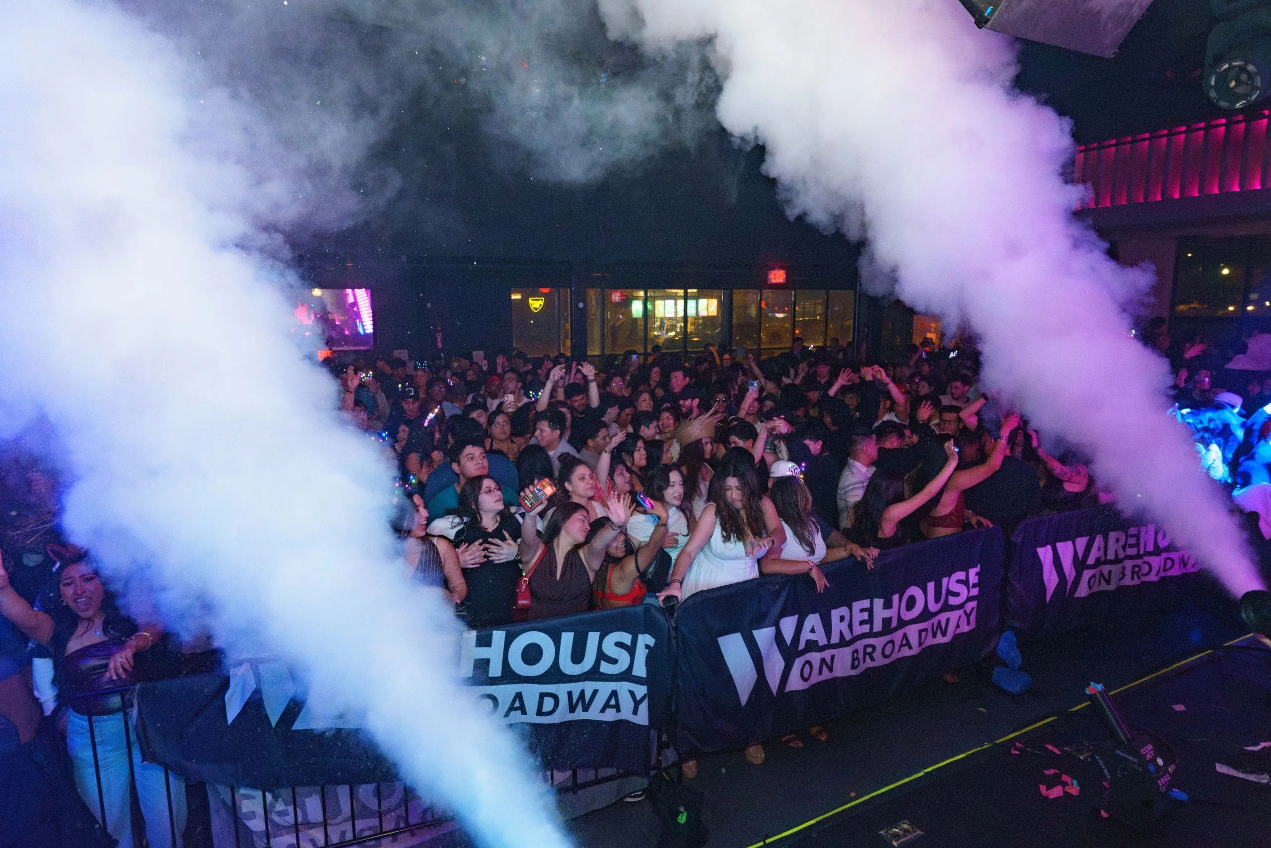 CO2 jets firing over a packed dance floor in front of the Warehouse on Broadway stage banner.