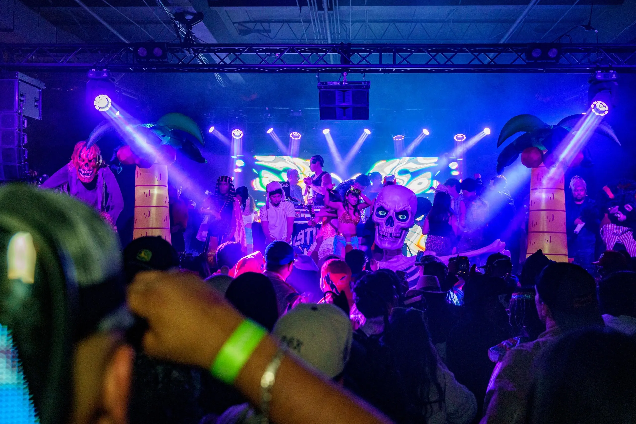The stage under blue and white beams with a giant inflatable skull and palm trees behind the DJ booth.